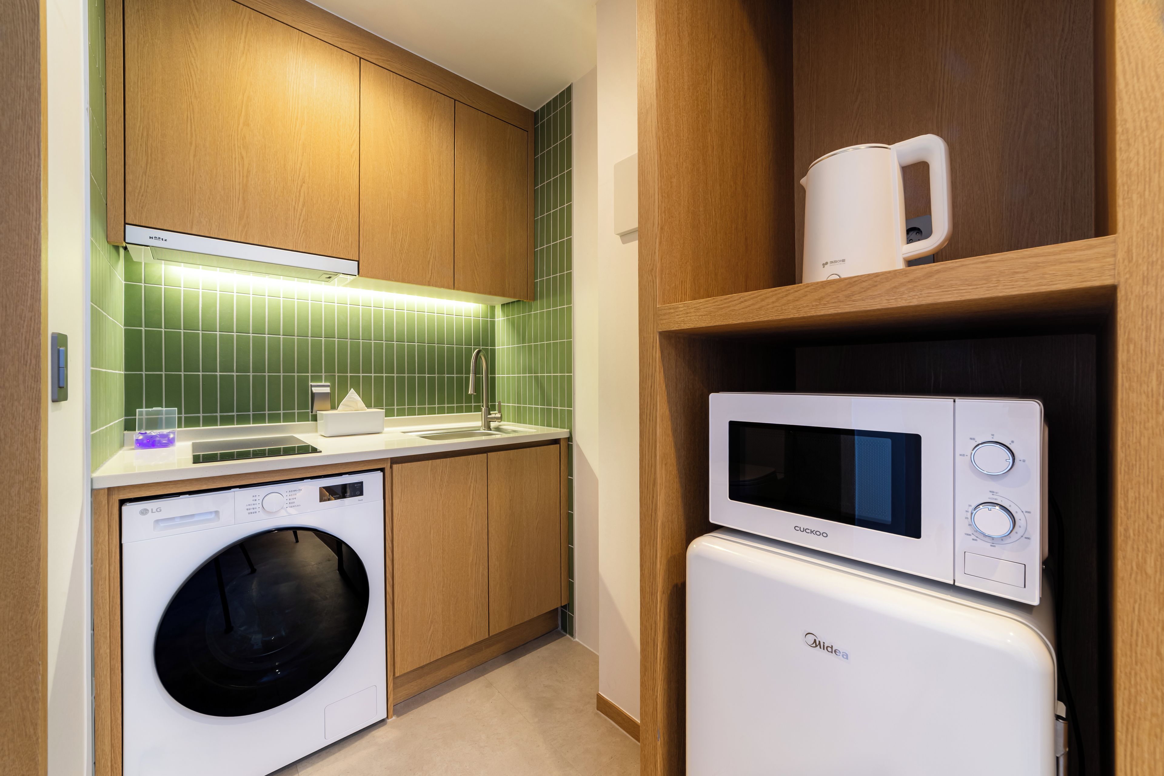 A compact kitchen with a washing machine, microwave, and a coffee maker on a shelf.