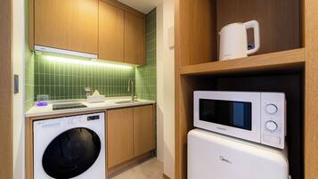 A compact kitchen with a washing machine, microwave, and a coffee maker on a shelf.