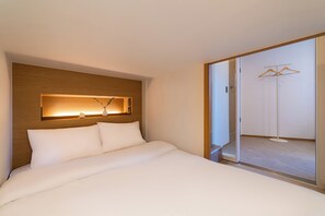 Quarto de hotel com cama, cabeceira de madeira, luminária fixa na parede e porta deslizante dando acesso a um armário.