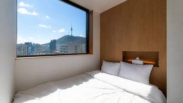 Habitación de hotel con cama, cabecera de madera, mesita de noche y ventana con vista a la ciudad.