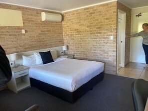 Ein Hotelzimmer mit Backsteinwand, einem Bett mit weißer Bettwäsche, einem Nachttisch mit Lampe und einer Tür zu einem anderen Raum.