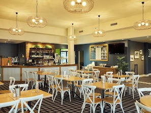 Ein Restaurant mit mehreren Tischen und Stühlen, einer Bar mit Theke und hängenden Leuchten.