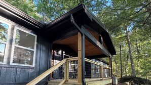 Eine Holztreppe führt zu einer überdachten Veranda mit Metallgeländer, umgeben von Bäumen.