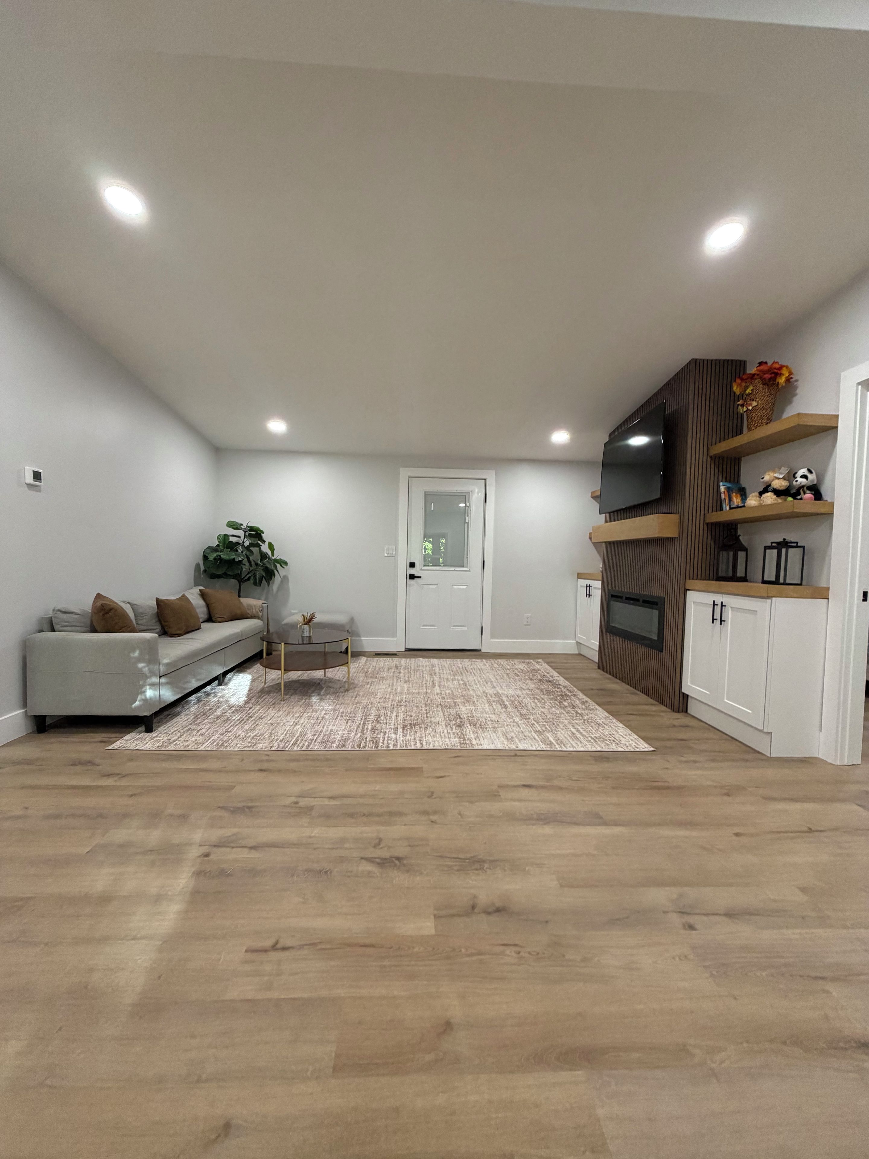 Een moderne woonkamer met een bank, een salontafel, een vloerkleed en ingebouwde houten kasten met een flatscreen televisie.