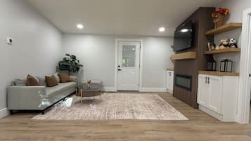 Een moderne woonkamer met een bank, een salontafel, een vloerkleed en ingebouwde houten kasten met een flatscreen televisie.