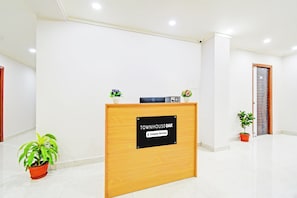 Mostrador de recepción con un cartel que indica servicio de la empresa. Hay plantas en macetas a ambos lados del mostrador.
