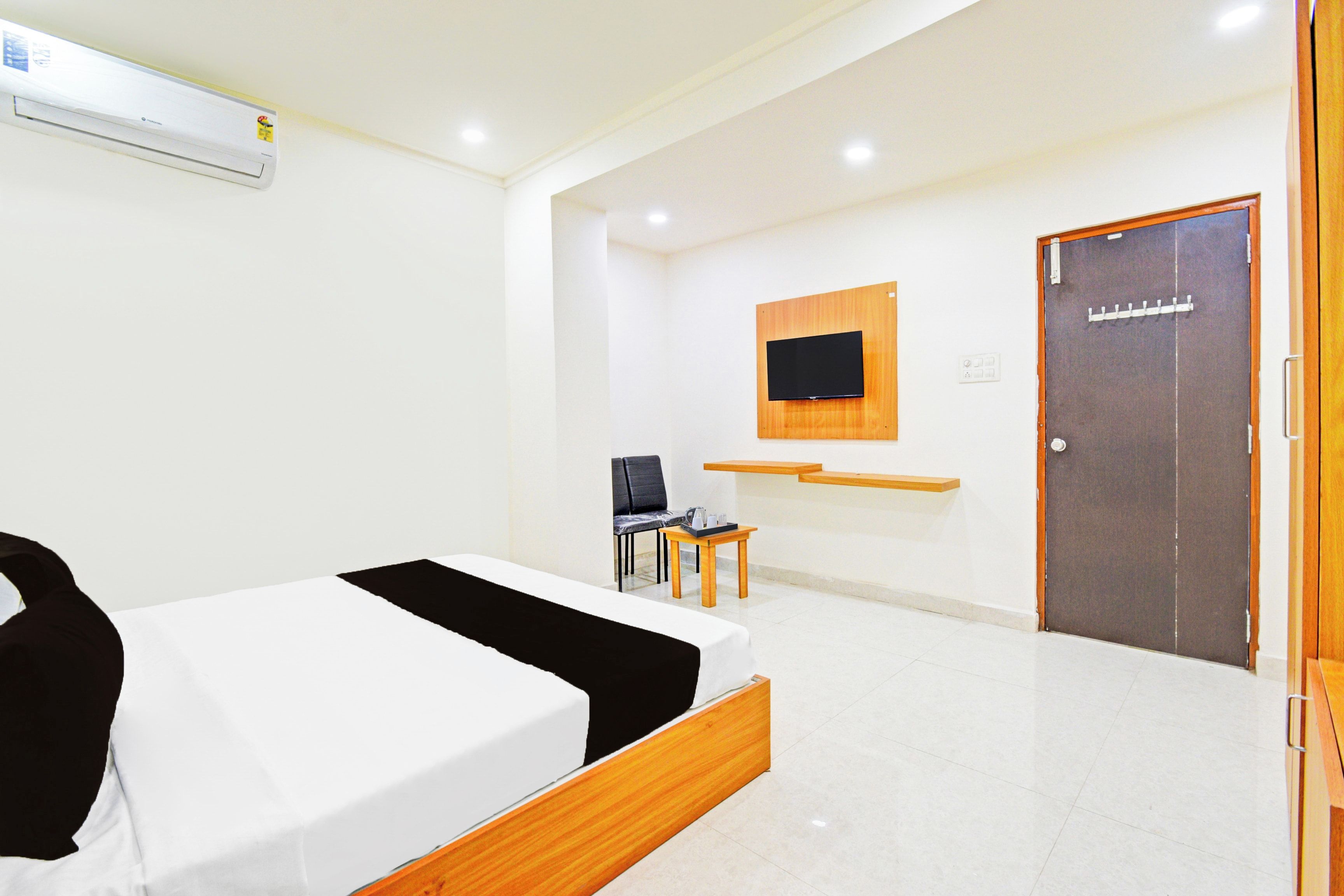 Une chambre d’hôtel comprenant un lit, un bureau, une chaise, un téléviseur fixé au mur et une porte.