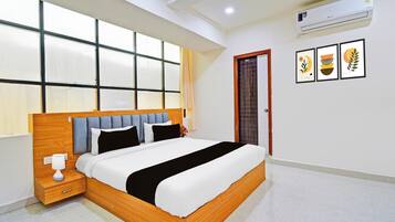 A modern bedroom with a large bed, a nightstand, a wall-mounted air conditioner, and framed artwork.