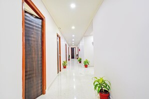 A corridor with doors, potted plants, and a tiled floor.