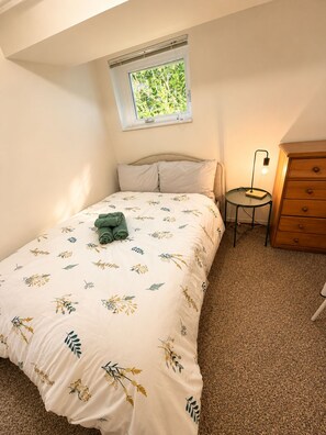Un dormitorio con cama, mesita de noche, cómoda y ventana con vista a la vegetación.