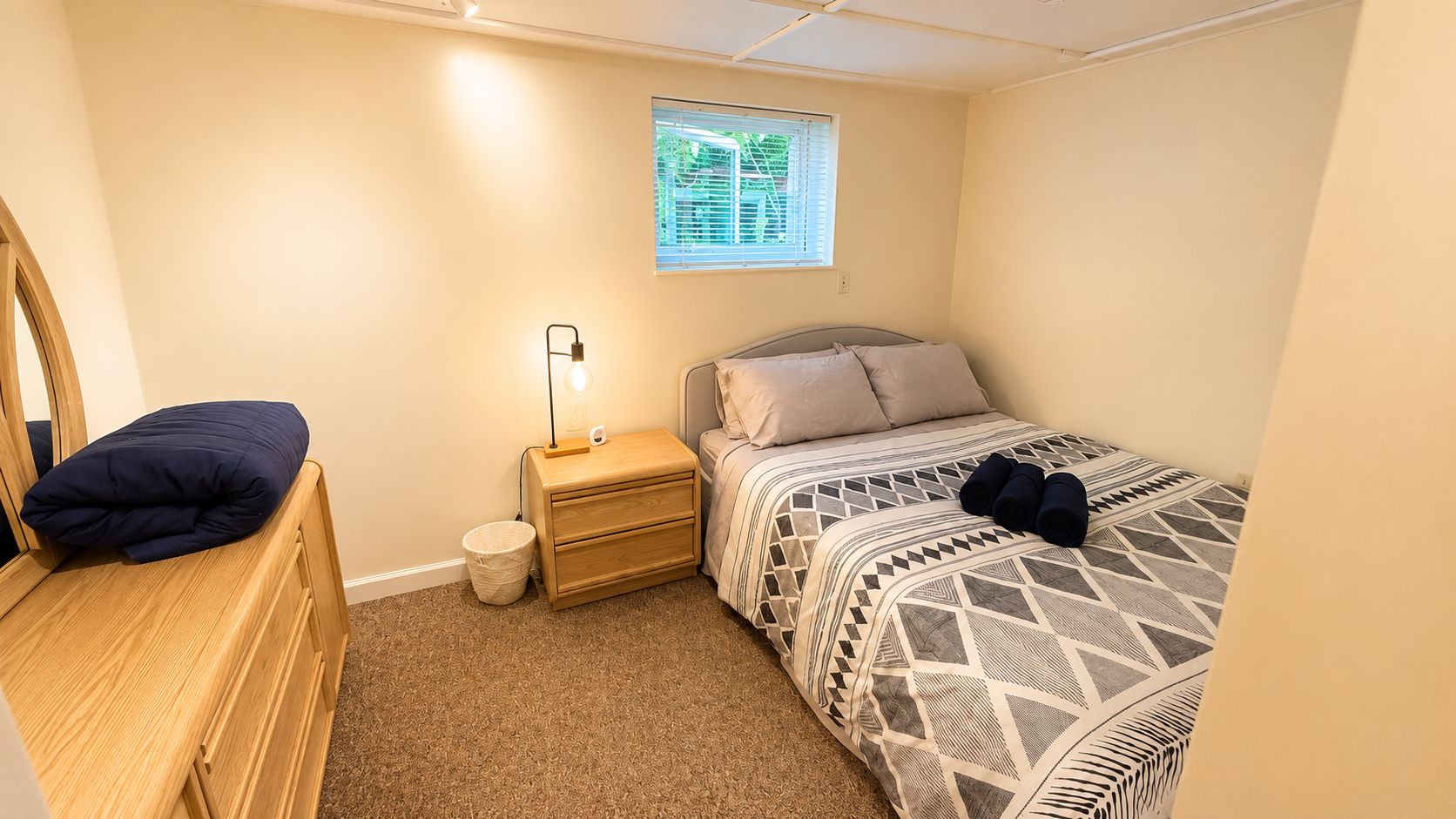 A bedroom with a bed, bedside table, lamp, and a window.