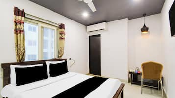Habitación de hotel con cama, una silla, escritorio, ventilador de techo y unidad de aire acondicionado.