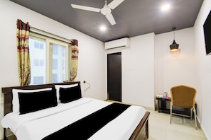 Habitación de hotel con cama, una silla, escritorio, ventilador de techo y unidad de aire acondicionado.
