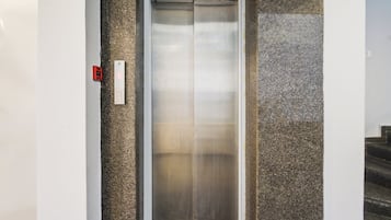 An elevator with a control panel on the left, a metallic door, and a textured wall on the right.