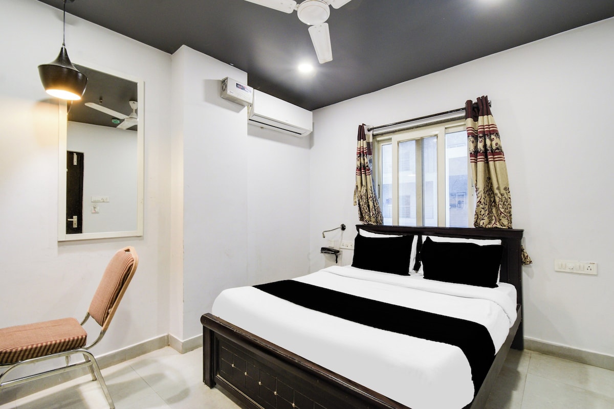 Un dormitorio con cama, una silla, ventilador de techo, aire acondicionado y ventana con cortinas.