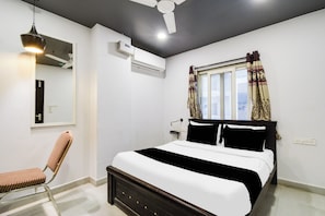 Un dormitorio con cama, una silla, ventilador de techo, aire acondicionado y ventana con cortinas.