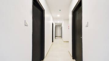 Um corredor comprido e estreito, com paredes brancas e portas pretas, que leva a um quarto no final.