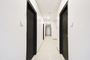 A long, narrow hallway with white walls and black doors, leading to a room at the end. - Super Townhouse Alwal Road (Hyderabad)