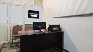 Pieni toimistotila, jossa on työpöytä, tuoli, tulostin ja kyltti, josta ilmenee, että tila on yrityksen käytössä.