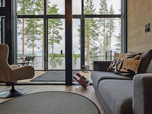 A modern living room with a sofa, armchair, and a view of a lake through large windows.
