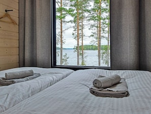 A room with two beds, a wooden wall, a window with a view of trees and water.