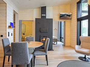 A modern interior with a round wooden table, grey upholstered chairs, a fireplace, and a large window with a view. - Jäkälänkallion ranta by Interhome (Äänekoski)