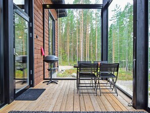 A wooden deck with a grill and outdoor furniture, overlooking a forest.