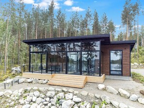 A modern cabin with a glass facade, wooden deck, and a forest backdrop. - Jäkälänkallion ranta by Interhome (Äänekoski)