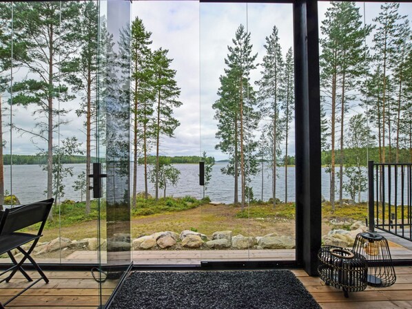A modern interior with large glass doors leading to a lakeside view, a black chair, and a small table with a black rug.