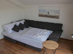 A modern room with a grey sofa bed, a small round table, and a painting of a beach scene on the wall. - Apartments Rivijera 1- One Bedroom Apartment III (Crikvenica)