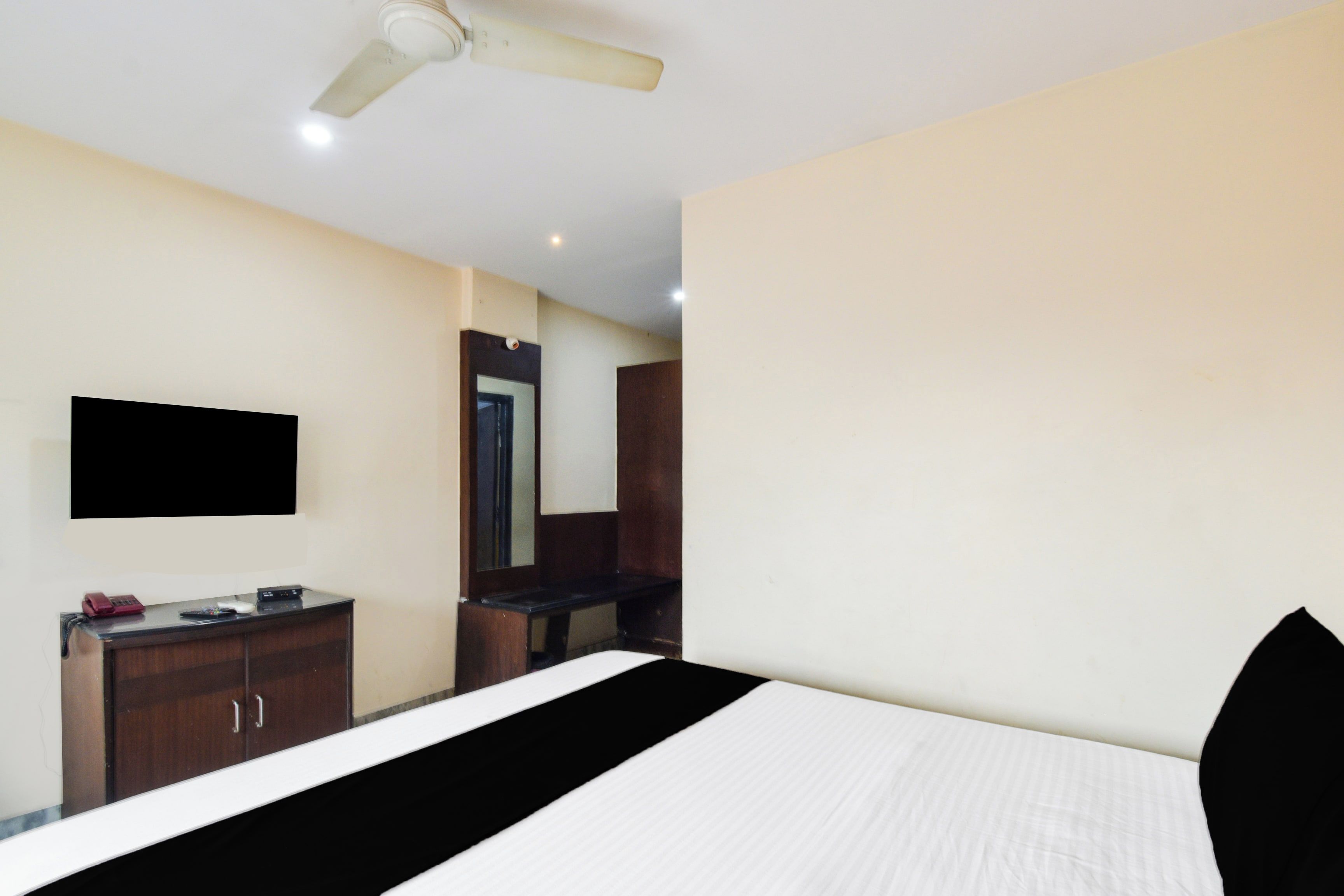 A hotel room with a bed, a desk with a telephone and a computer, a mirror, and a ceiling fan.