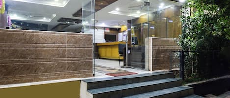 A hotel lobby with a reception desk, a staircase leading to an upper floor, and a glass partition.