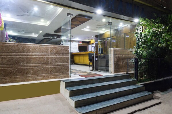 A hotel lobby with a reception desk, a staircase leading to an upper floor, and a glass partition.