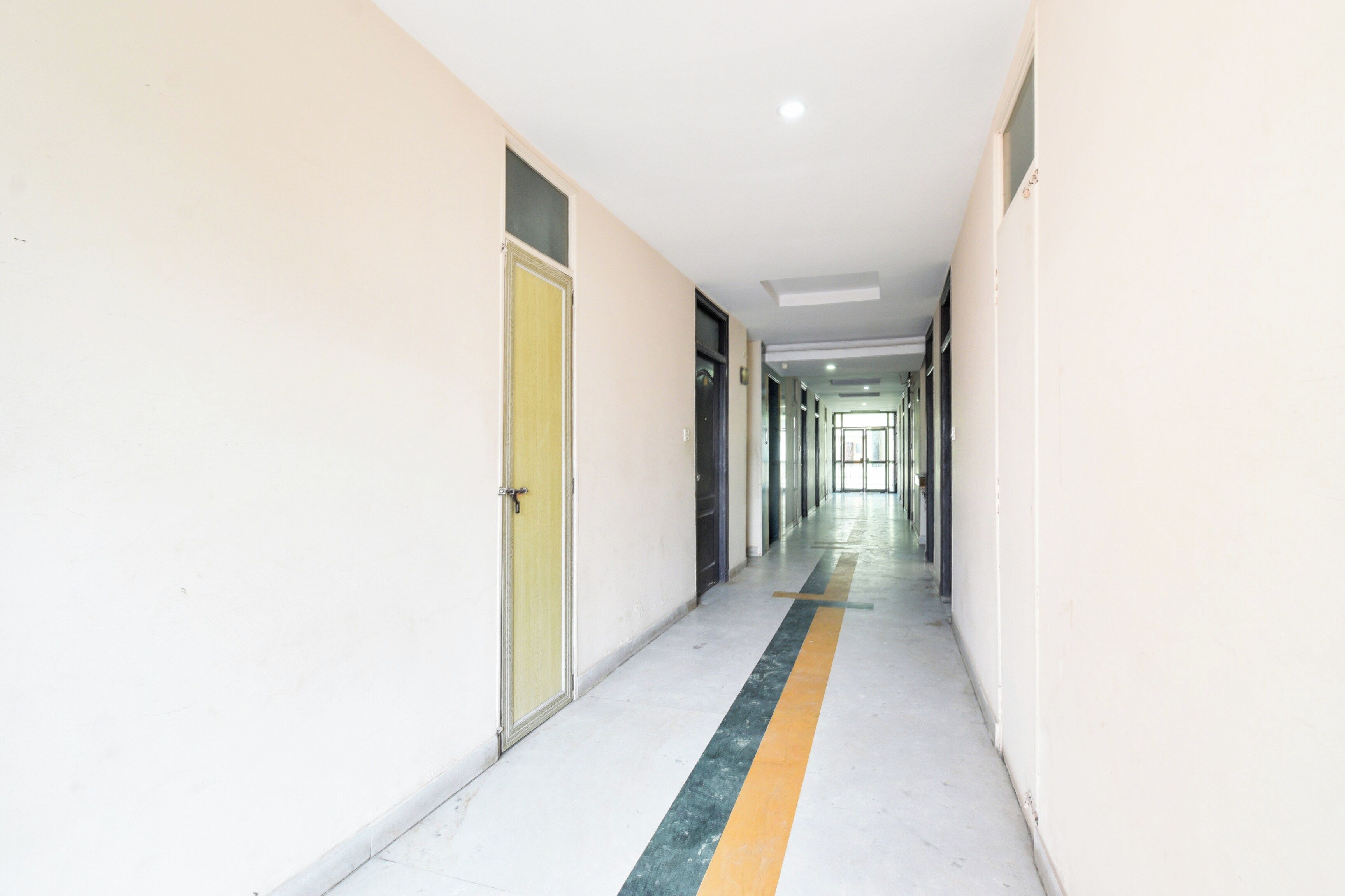 A long, narrow hallway with doors on both sides, a yellow stripe on the floor, and a ceiling light.