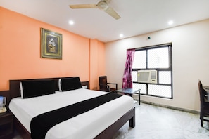Habitación de hotel con cama, escritorio, silla, ventilador de techo, aire acondicionado y ventana con cortinas.