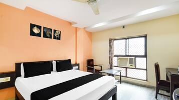 Una habitación de hotel con una cama, un ventilador de techo, una ventana con aire acondicionado y una mesita.
