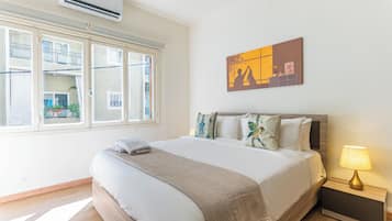 Una habitación de hotel con cama, mesita de noche, lámpara, ventana y una obra de arte en la pared.