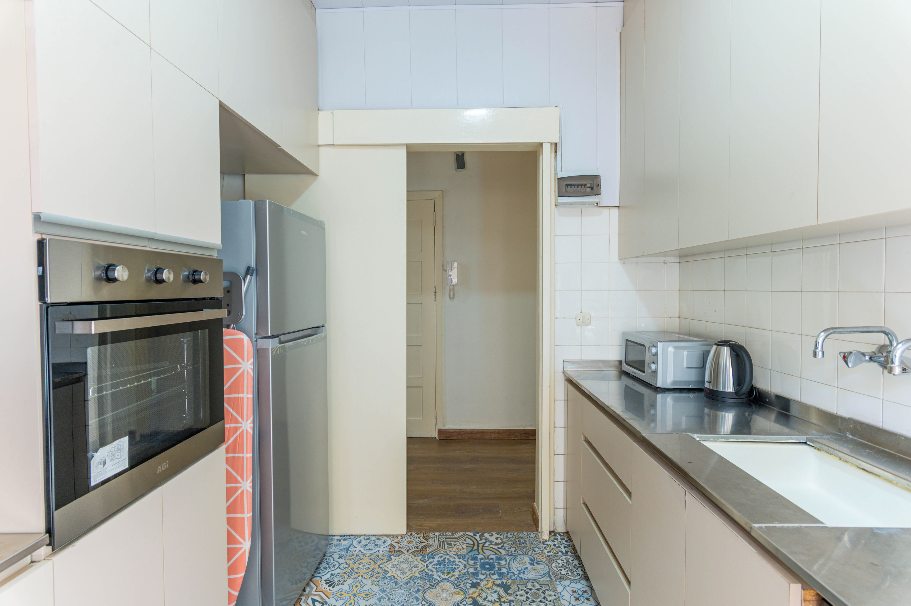 A compact kitchen with a built-in oven, a microwave, a toaster, and a kettle.
