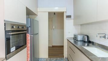 A compact kitchen with a built-in oven, a microwave, a toaster, and a kettle.