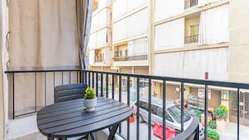 Un balcón con una mesa redonda y sillas, una planta en maceta y vistas a un edificio de varios pisos con balcones.