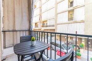 A balcony with a round table and chairs, a potted plant, and a view of a multi-story building with balconies. - Rue - 2-BR Apt. & Balcony in Mar Mikhael (Beirut)