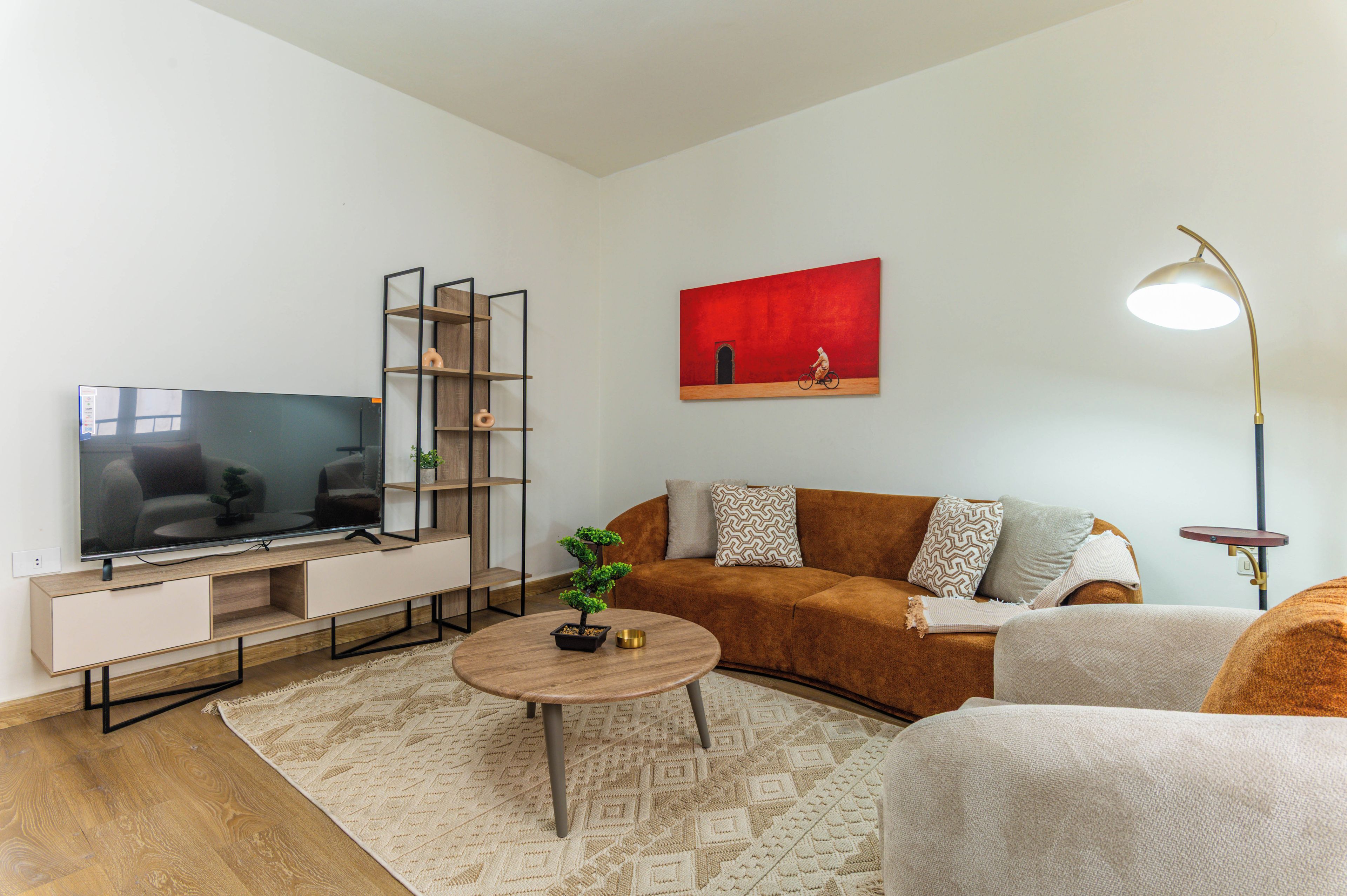 A modern living room with a flat-screen TV, a sofa, a coffee table, and a painting on the wall.