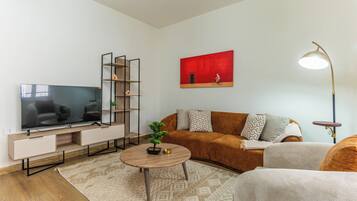 A modern living room with a flat-screen TV, a sofa, a coffee table, and a painting on the wall.
