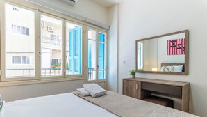 A hotel room with a bed, a wooden dresser, a mirror, and a window with shutters. - Rue - 2-BR Apt. & Balcony in Mar Mikhael (Beirut)