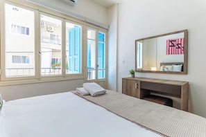 A hotel room with a bed, a wooden dresser, a mirror, and a window with shutters. - Rue - 2-BR Apt. & Balcony in Mar Mikhael (Beirut)