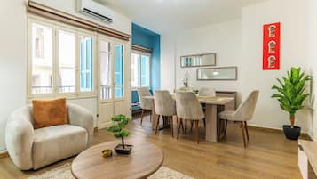 Una sala de estar moderna con un sofá, una mesa de comedor con sillas, una pequeña planta en maceta y una mesa de centro redonda.