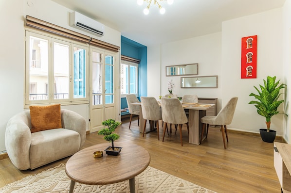 A modern living room with a sofa, a dining table with chairs, a small potted plant, and a round coffee table. - Rue - 2-BR Apt. & Balcony in Mar Mikhael (Beirut)