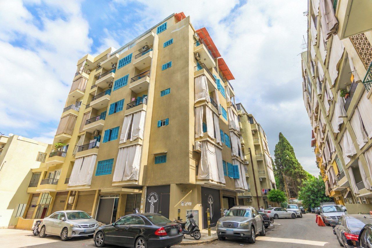 Un edificio residencial de varios pisos con balcones, coches estacionados y cielo despejado.