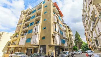 Un edificio residencial de varios pisos con balcones, coches estacionados y cielo despejado.