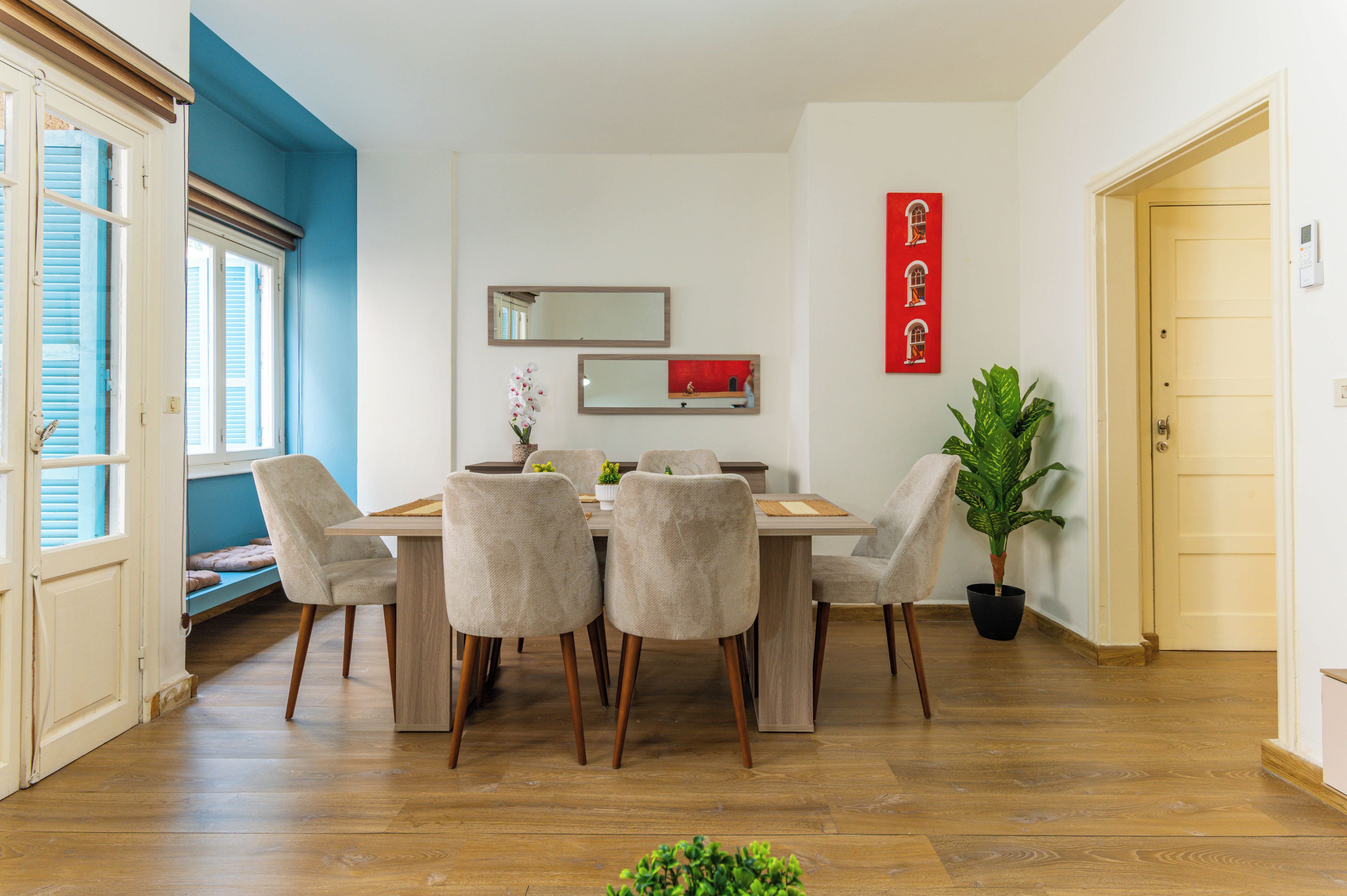 A dining area with a wooden table and chairs, a potted plant, and a wall-mounted mirror.